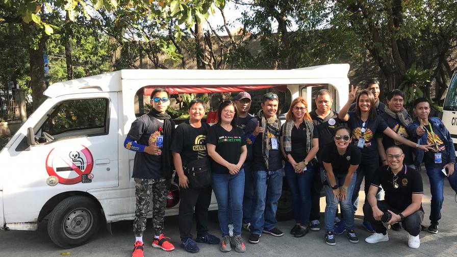 A large group stand in front of a bus with a no smoking sign on the door