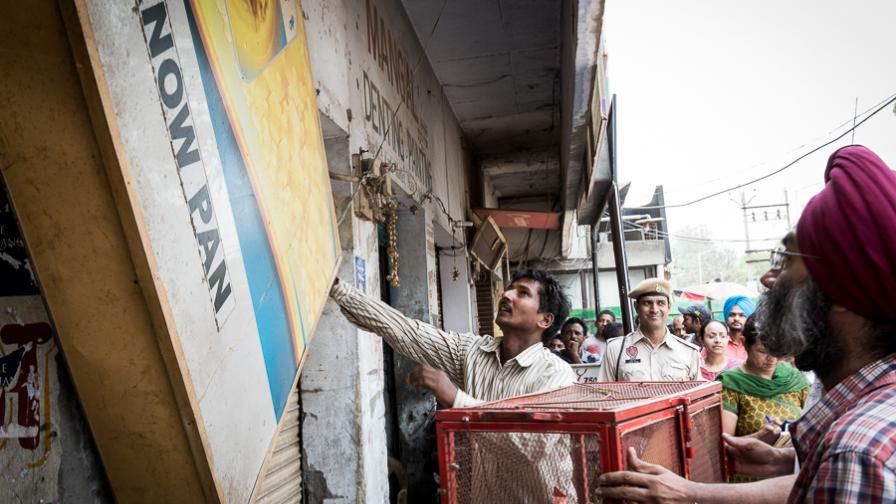 Several people remove a large tobacco advertising board from a storefront